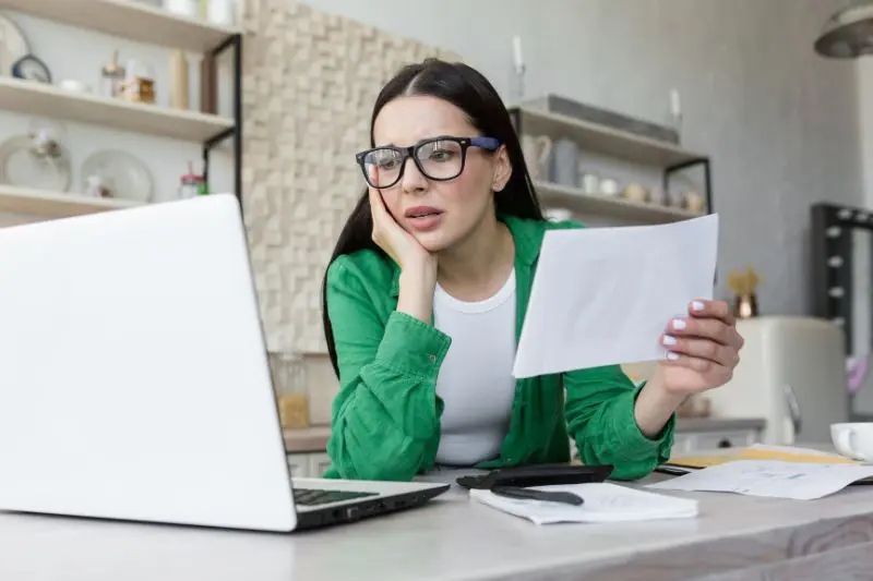 upset woman looking at document and computer