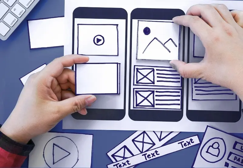 Hands arranging paper wireframes and sketches for mobile dental website design on a desk
