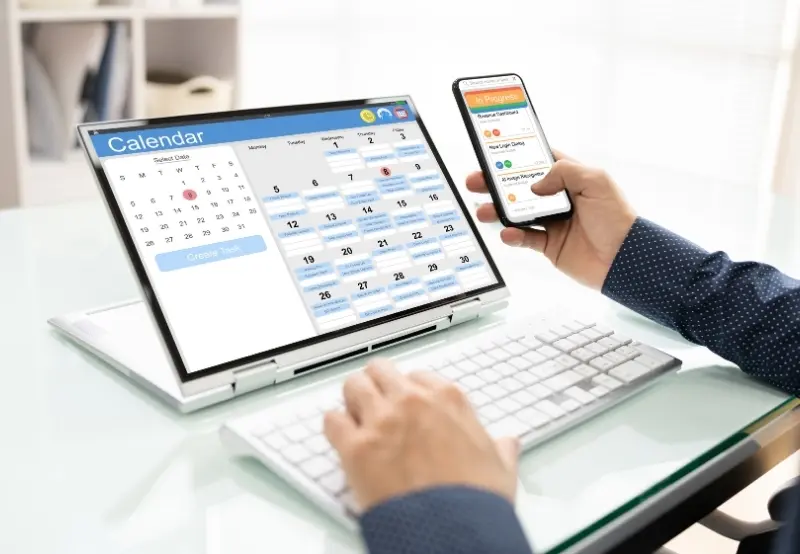 Dentist managing online appointment scheduling calendar on laptop and mobile device